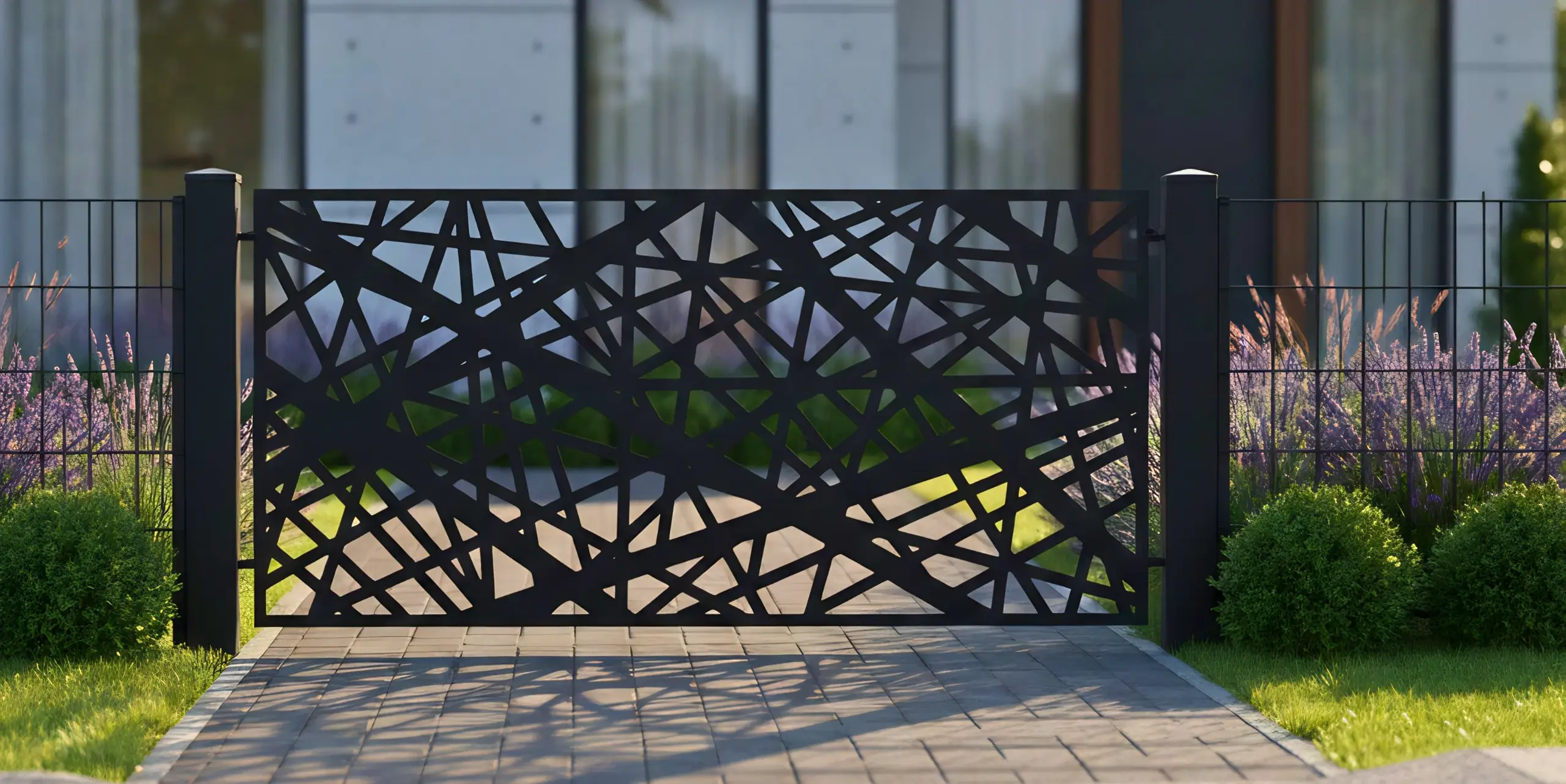Czarny, ażurowy płot z geometrycznym wzorem stojący przy chodniku, z ogrodem i roślinami w tle.
