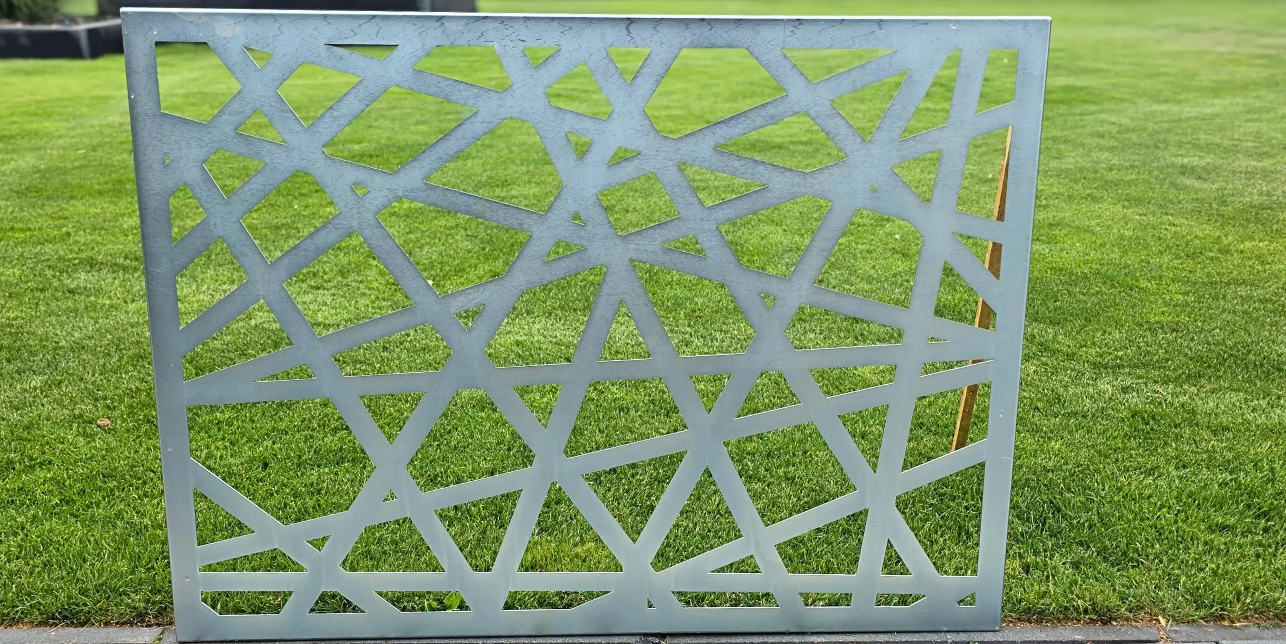 Ażurowy panel z geometrycznym wzorem ustawiony na świeżo skoszonej trawie.