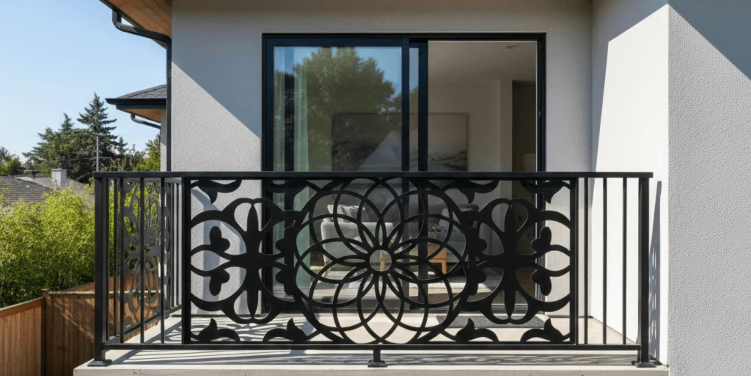 Mały balkon z ozdobną metalową balustradą i przeszklonym wejściem do jasnego wnętrza domu.