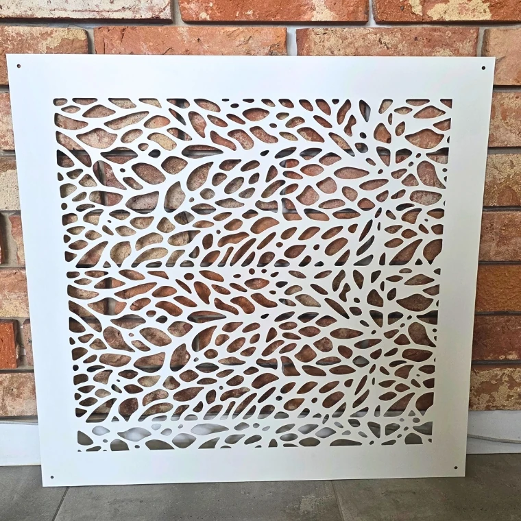 Metalowy panel ozdobny z organicznymi wycięciami, ustawiony przy ścianie